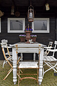Gartenstühle am Tisch mit Vintage-Deko vorm schwarzen Holzhaus