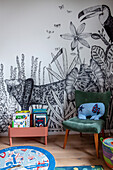Bookcase and upholstered chair in front of wallpaper with jungle motif in children's room