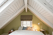 Double bed with scatter cushions in attic bedroom with white-painted wooden ceiling