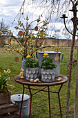 Ländliche Osterdeko auf Tisch im Garten mit Ranunkeln, Strauß aus Weidenkätzchen, Osterhase und Ostereiern