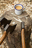 Axes on tree trunk and tea mug in a carpenter's workshop