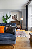 Grey upholstered sofa, in the background antique bench and painting of a rabbit in a wall niche