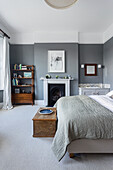 Queen bed, wooden chest, fireplace and mid-century bookcase in a bedroom with grey walls