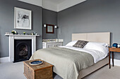 Double bed, wooden chest and fireplace in the bedroom with grey walls