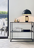 Filigree, black console with table lamp in front of white wall