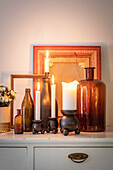 Deko aus Kerzen und Glasflaschen auf weißer Kommode mit Bilderrahmen