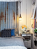Bedroom corner with rustic metal wall decoration, bed, bedside table and hanging lamp