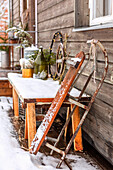 Winterliches Dekor und alter Holzschlitten im Schnee vor Holzhaus