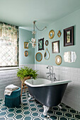 Freestanding bathtub with lion feet in bathroom with wall mirrors and pastel green wall