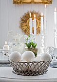 Metal basket with white eggs, in the background burning candles on an Easter table