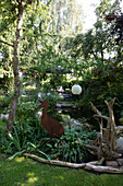 Deko aus Edelrost und Treibholz am Teich im üppig bewachsenen Garten