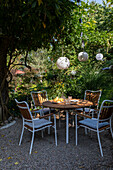 Round patio table with chairs on a gravel patio, lanterns above in garden