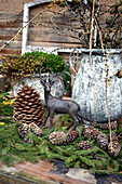 Deer figurine, conifer branches and cones in front of old pots on garden table