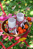 Candles decorated with spindle seed heads and physalis in a bowl