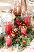 Weihnachtstisch-Dekoration mit Tannezweigen, roten Beeren, roten Kerzen und Walnüssen