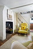 Living room with yellow armchair, fireplace and white wooden staircase