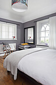 Schlafzimmer mit weißer Bettwäsche, grauen Wänden und Holzboden