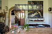 Rustikales Esszimmer mit Holztisch, länglicher Pendelleuchte und klassischem Gemälde