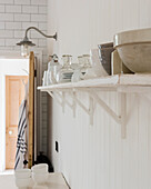 White kitchen shelf with crockery and country-style wall paneling