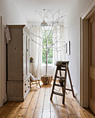 Hallway with white wooden cupboard, tree and wooden ladder as decorative elements