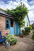 Idyllische Gartenecke mit Wisteria an einer Ziegelsteinwand und blauer Holzfassade