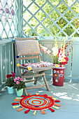DIY-Flickenteppich aus bunten Stoffresten, Dahlien, Gladiolen und Holzstuhl mit Kissen auf dem Balkon