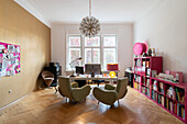 Bright study with herringbone parquet flooring, green armchairs and pink shelves