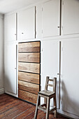 White built-in cabinets with wooden drawers in minimalist design and old wooden chair