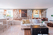 Wohnzimmer mit freiliegendem Mauerwerk, weißem Sofa und dunkler Holztruhe als Tisch