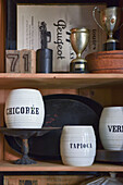 Labelled ceramic storage pots and antique trophies in cabinet