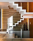 White staircase with modern glass railing in front of wood panelling in a flat