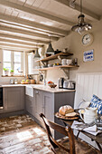 Country kitchen with grey cabinets, vintage pendant lights and covered dining table