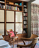 Lesezimmer mit Bücherregal, Holzstühlen und gemustertem Vorhang