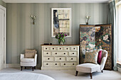 Schlafzimmer mit gemusterter Tapete, cremefarbener Kommode und Raumteiler mit Blumenmuster