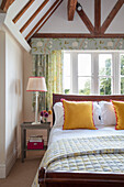 Schlafzimmer mit Holzbalken, floralen Vorhängen und farbigen Akzenten