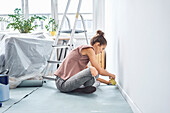 Young woman applying adhesive tape on wall while sitting at home