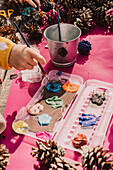 Hand of girl mixing watercolor on palette with paintbrush at picnic table in park during sunny day