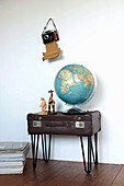 Globe and figurines standing on side table made of old suitcase, with old camera hanging on wall