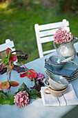 Crockery and DIY lamp shade made of leaves and hydrangea flowers lying on coffee table set in garden
