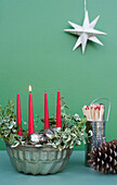 Studioaufnahme von DIY-Adventsdekorationen mit Kerzen, Zweigen, Tannenzapfen, Streichhölzern und Backform