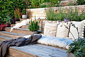 Seating area on wooden terrace with cushions and plants in the background