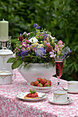 Romantisch gedeckte Kaffeetafel im Mai, mit einem Wiesenblumenstrauß, Erdbeeren und Erdbeertörtchen