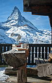 Blick auf schneebedecktes Matterhorn, Bank aus Holz, Tisch aus halbem Baumstamm, Bücher und Kaffeetassen