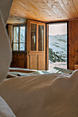 Blick auf schneebedeckte Berge aus einem rustikalen Holzschlafzimmer