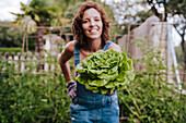 Lächelnde Mitte erwachsene Frau mit Salat im Stehen im Gemüsegarten