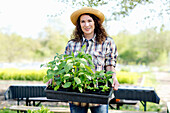 Portrait of smiling mature woman holding tray with green plants at community garden