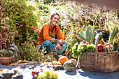 Lächelnde Frau, die Obst und Gemüse erntet, während sie im Garten sitzt