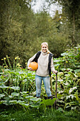 Portrait of smiling young woman with spade and pumpkin in garden
