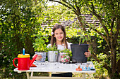 Portrait of proud little girl with potted spice plants on table in the garden