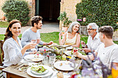 Glückliche Familie, die zusammen im Garten isst, Gläser klirrend